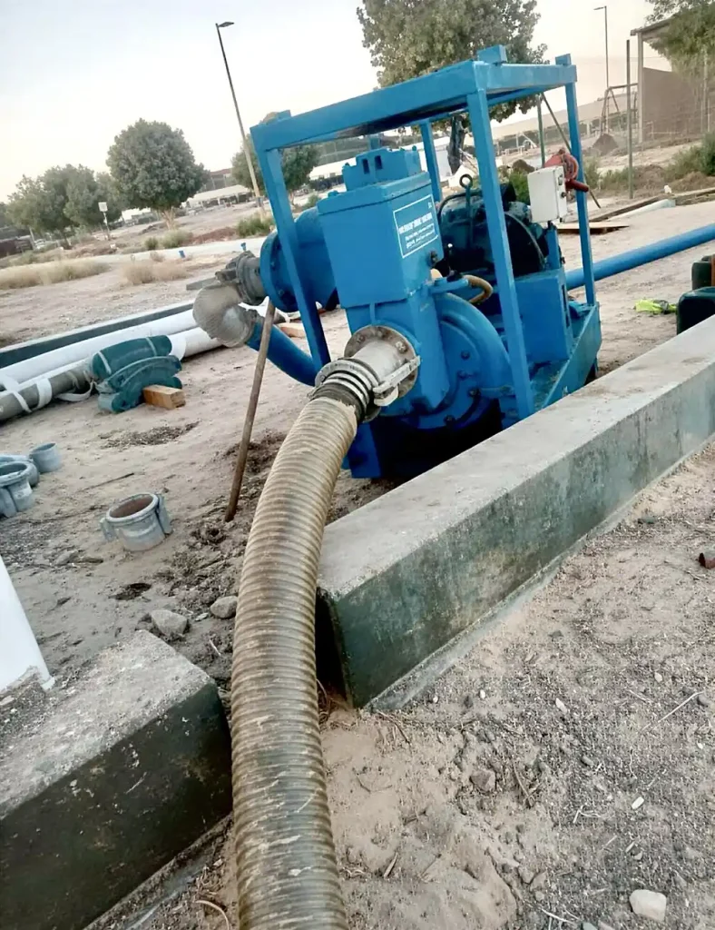 A view of a Sykes GP150 pump showing the rugged discharge connection and lay-flat hose routed across the construction site.