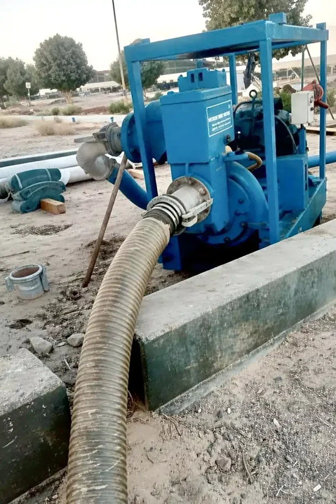 A view of a Sykes GP150 pump showing the rugged discharge connection and lay-flat hose routed across the construction site.